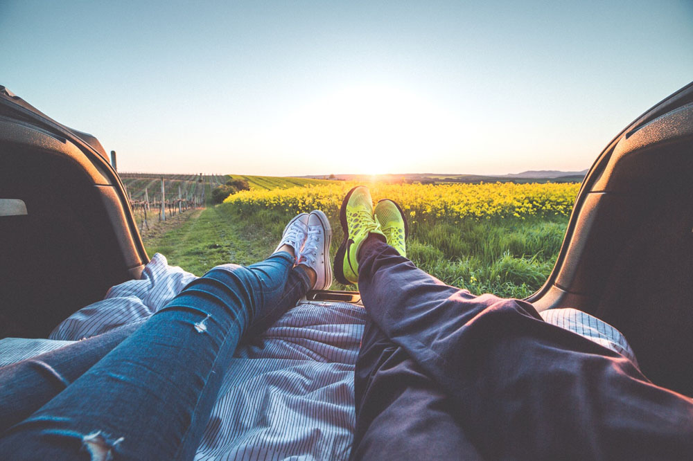 A pair of individuals lounging in the backseat of a car with their feet elevated.