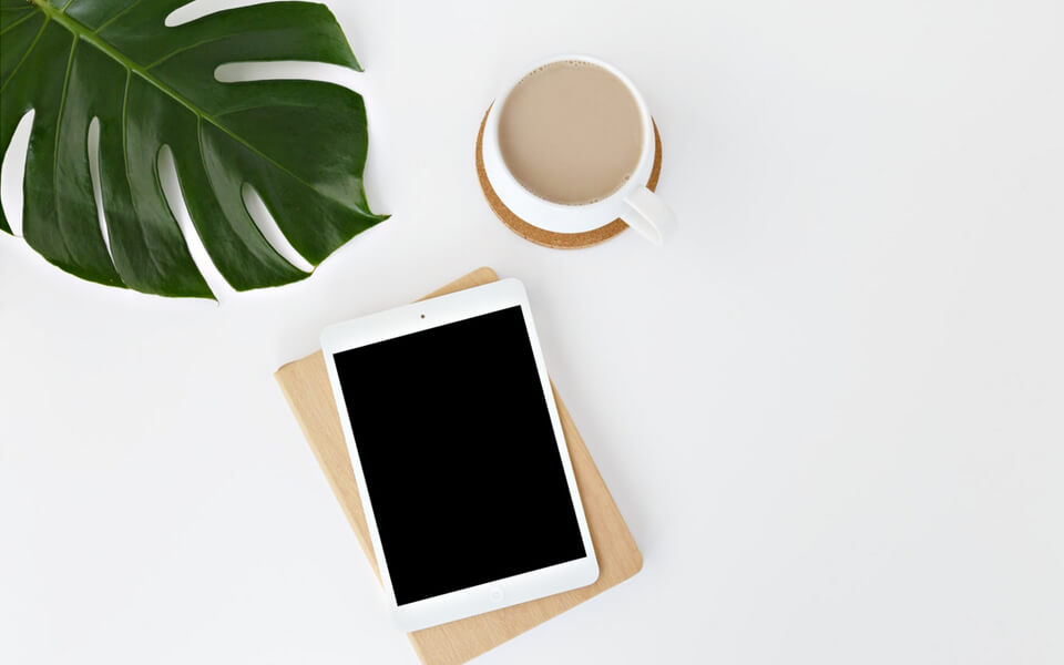 A coffee cup sits next to a tablet with a blank screen on a clean white background.
