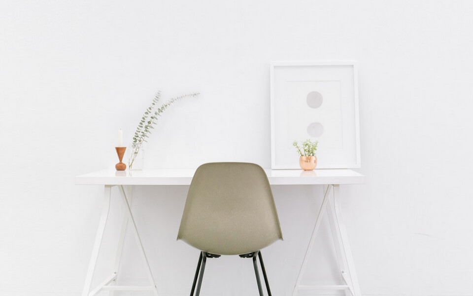 An image of a white desk and chair positioned in front of a plain white wall.